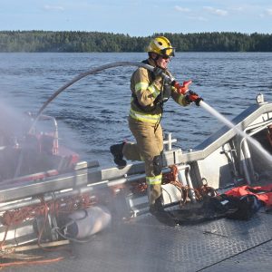 Pelastaja sammutusruiskun kanssa astumassa veneen kannelle.